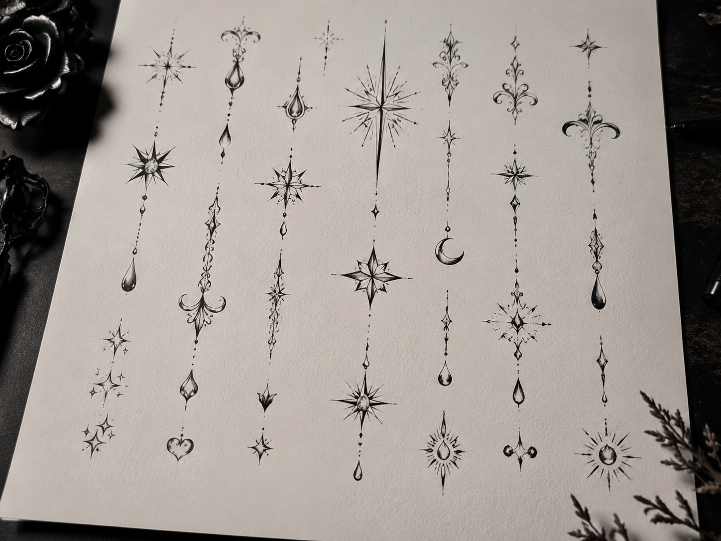 Tattoo flash sheet of face tattoo design ideas with fine line ornamental symbols, stars, crescent and teardrop placements in black ink on studio paper