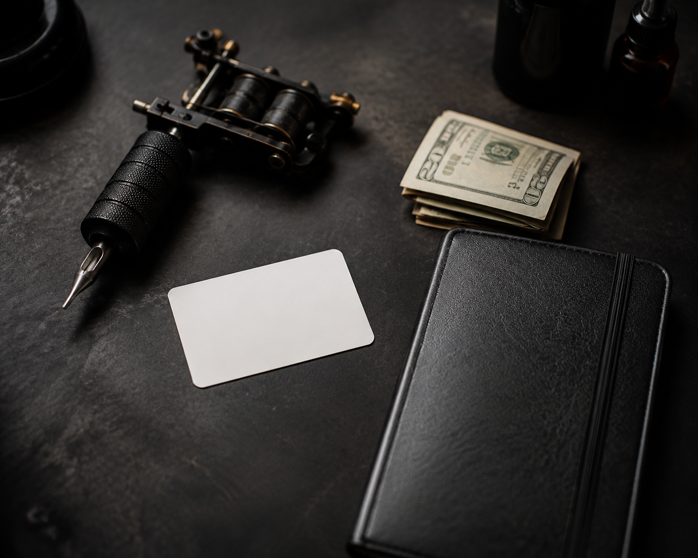 Tattoo machine, blank booking card, folded cash and an appointment book on a dark studio counter