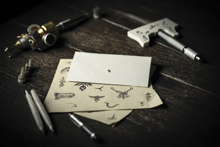 Tattoo flash sheets, a tattoo machine and needle cartridges laid out on a dark studio table