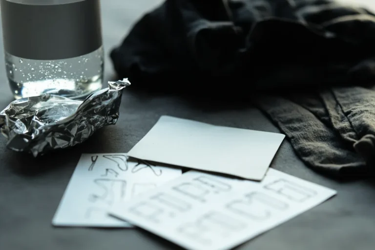 Tattoo appointment essentials on a table: water bottle, folded dark clothing, reference sheets and a foil-wrapped snack